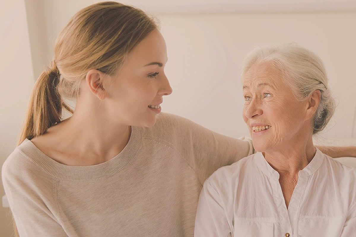 A caregiver and an older woman smiling together at home